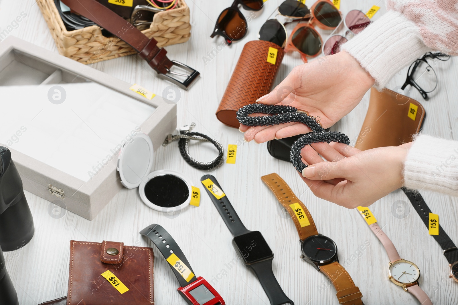Photo of Woman holding bracelet near table with different stuff, closeup. Garage sale