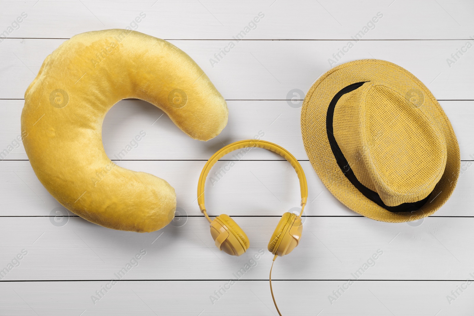 Photo of Yellow travel pillow, hat and headphones on white wooden background, flat lay