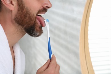 Man brushing his tongue with cleaner in bathroom, closeup. Space for text