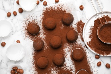 Delicious chocolate truffles with cocoa powder and hazelnuts on white marble table, flat lay