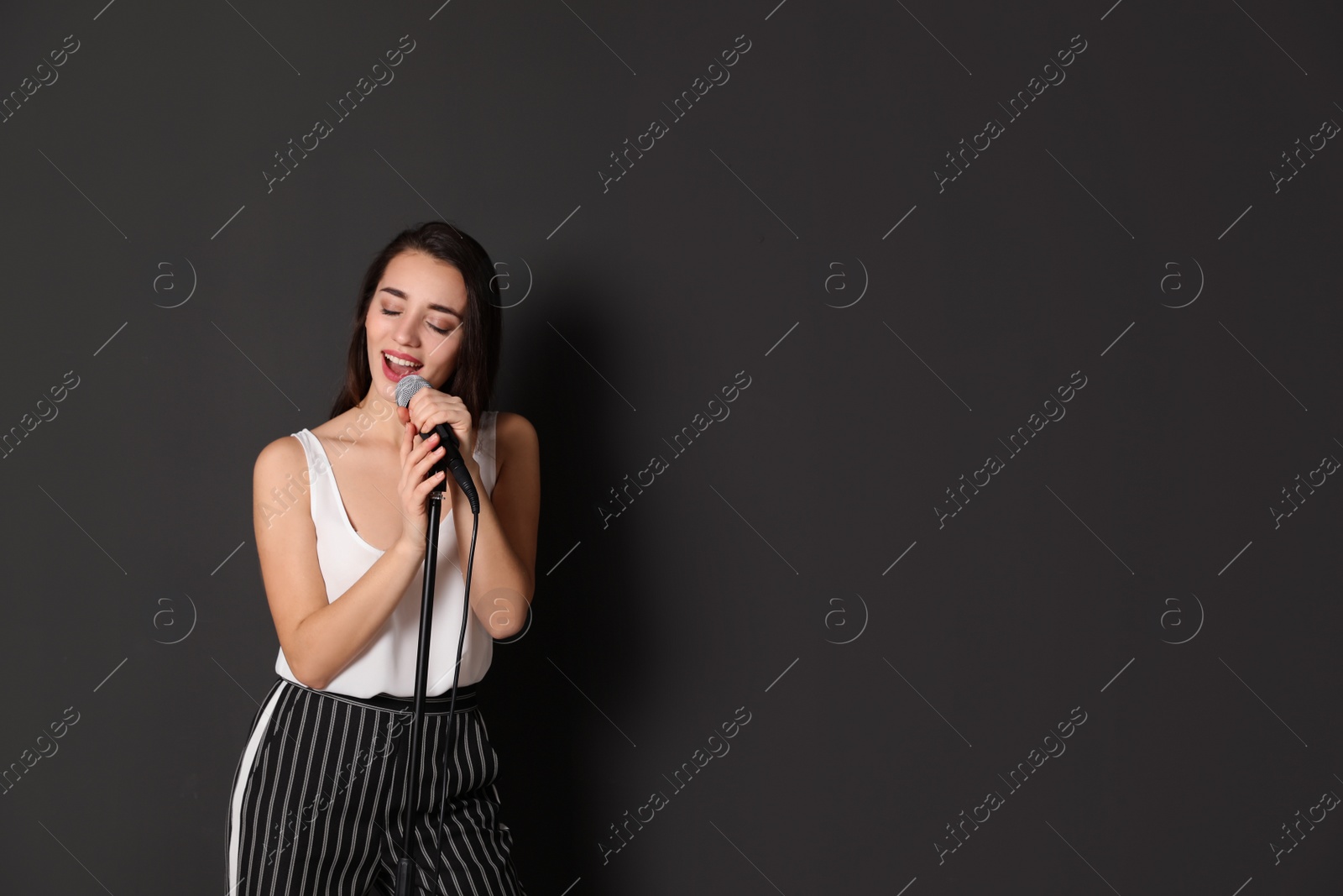 Photo of Young stylish woman singing in microphone on dark background. Space for text