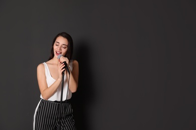 Photo of Young stylish woman singing in microphone on dark background. Space for text