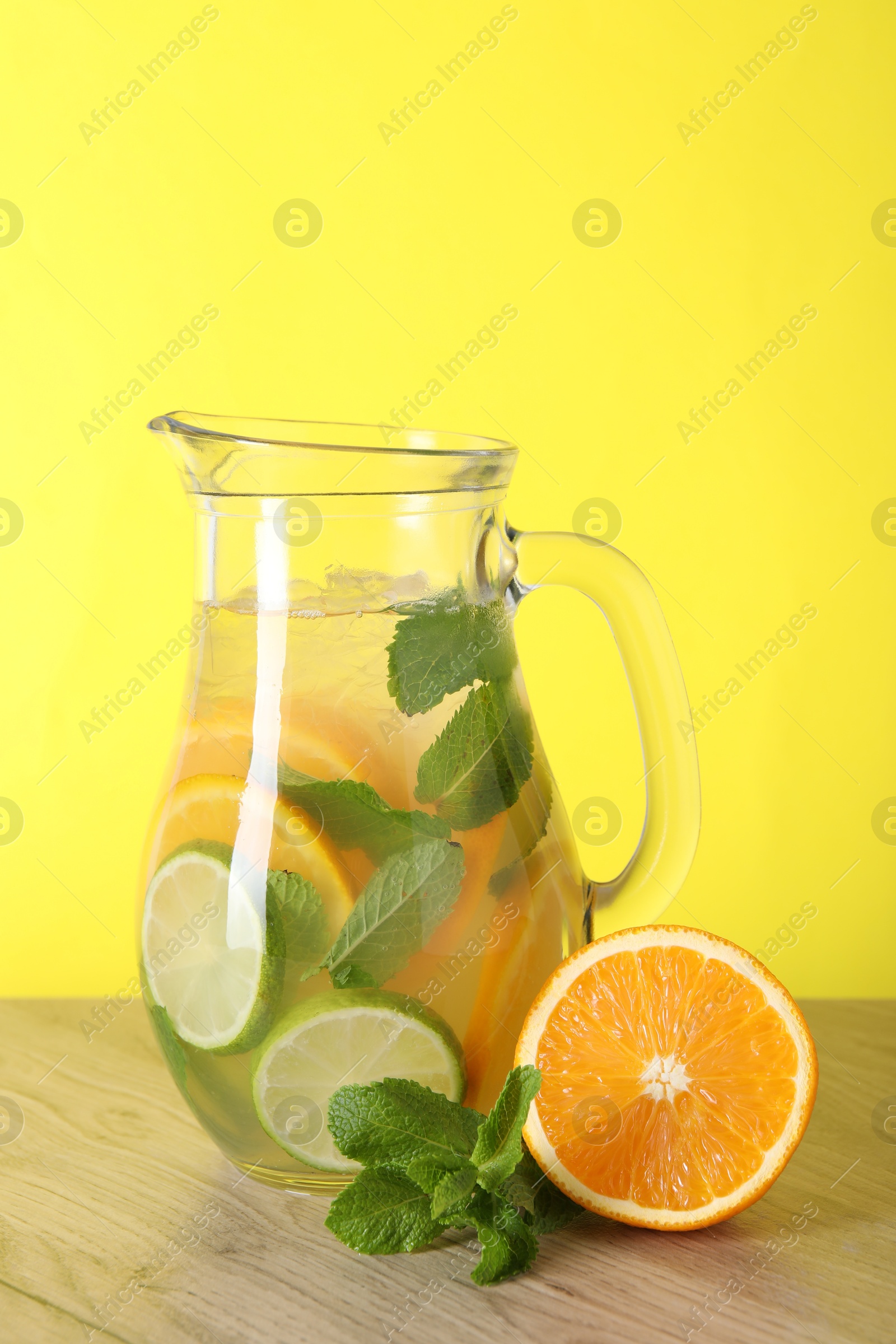 Photo of Freshly made lemonade with mint in jug on wooden table against yellow background