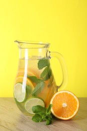 Freshly made lemonade with mint in jug on wooden table against yellow background