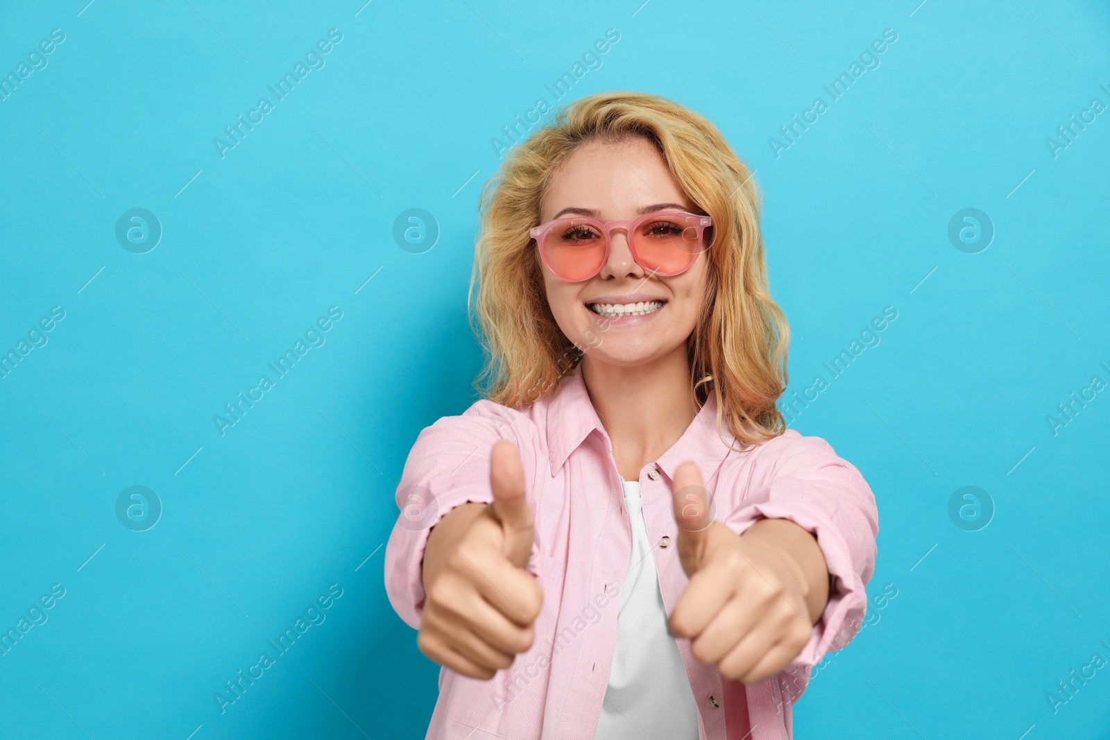 Photo of Happy young woman showing thumbs up on light blue background