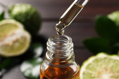 Photo of Bergamot essential oil dripping from pipette into bottle on blurred background, closeup