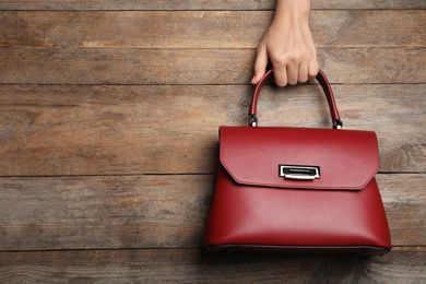 Photo of Woman holding small bag on wooden background, top view. Space for text