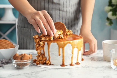 Photo of Young woman decorating delicious caramel cake at table