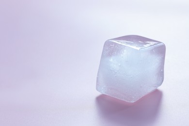 Crystal clear ice cube on light pink background, space for text