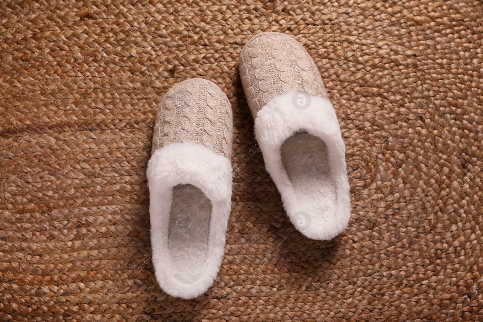 Photo of Pair of warm stylish slippers on wicker carpet, top view