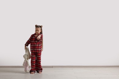 Photo of Girl in pajamas with toy bunny sleepwalking indoors, space for text