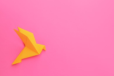 Photo of Beautiful orange origami bird on pink background, top view. Space for text