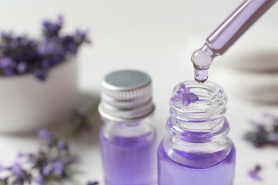 Dripping natural cosmetic oil into glass bottle with lavender flower on blurred background, closeup. Space for text