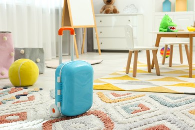 Photo of Light blue toy suitcase on rug in playroom. Kindergarten interior design