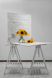 Photo of Glass vase with beautiful sunflowers and double-sided backdrop on table in photo studio