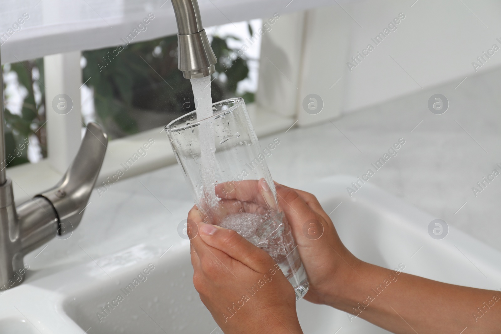 Photo of Girl filling glass with water from tap at home, closeup