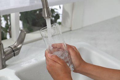 Girl filling glass with water from tap at home, closeup