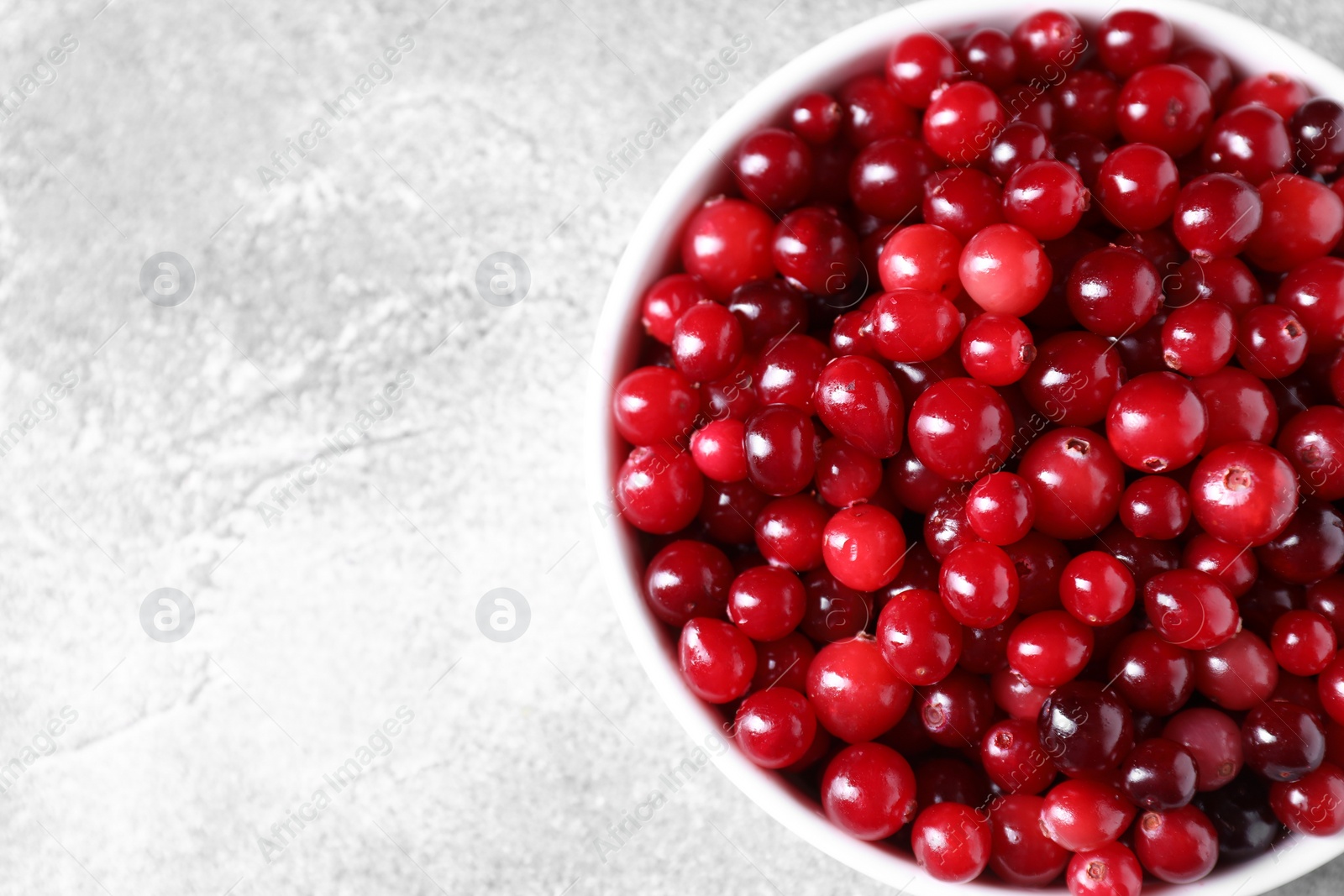 Photo of Fresh ripe cranberries in bowl on grey table, top view. Space for text