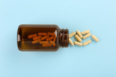 Photo of Bottle and vitamin capsules on light blue background, top view