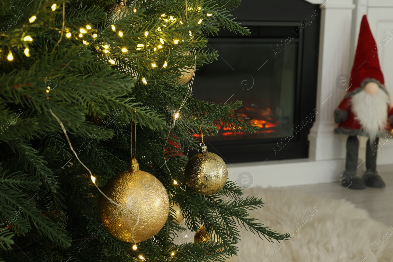 Photo of Christmas tree decorated with ornaments and festive lights near fireplace in room, closeup