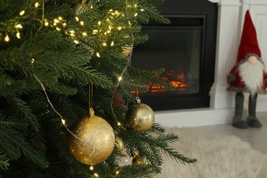 Photo of Christmas tree decorated with ornaments and festive lights near fireplace in room, closeup