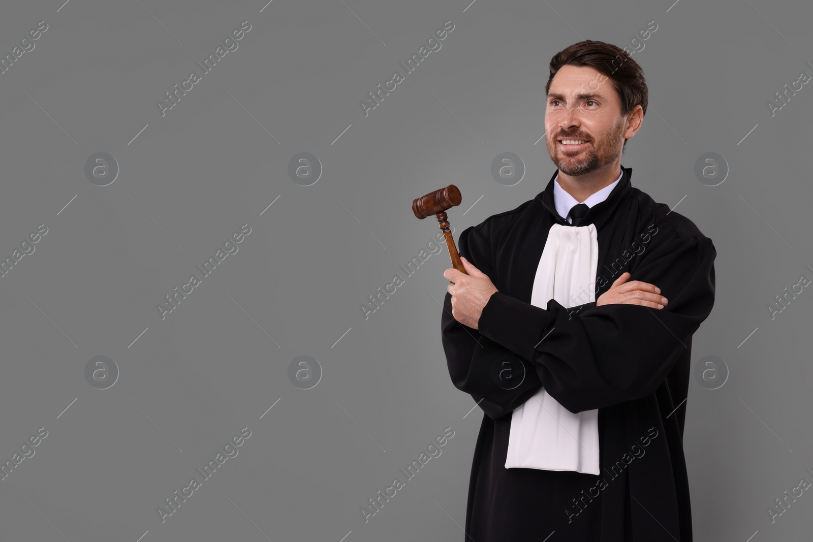 Photo of Happy judge with gavel on grey background. Space for text