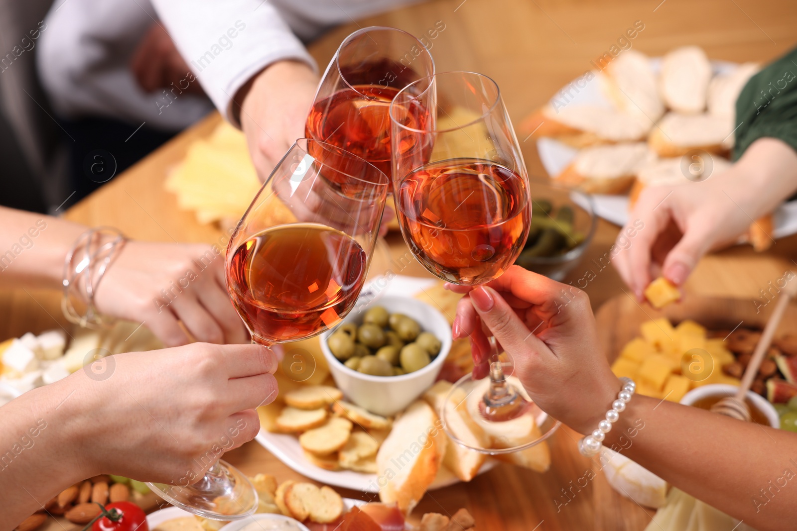Photo of People clinking glasses with rose wine above wooden table, closeup