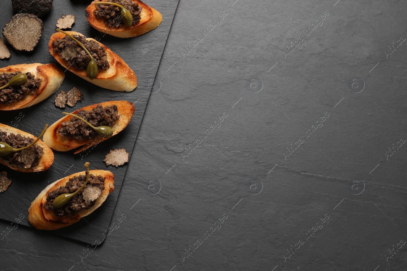 Photo of Tasty bruschettas with truffle paste and capers on black table, top view. Space for text