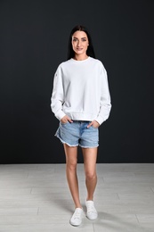 Photo of Full length portrait of young woman in sweater at black wall. Mock up for design