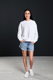 Full length portrait of young woman in sweater at black wall. Mock up for design