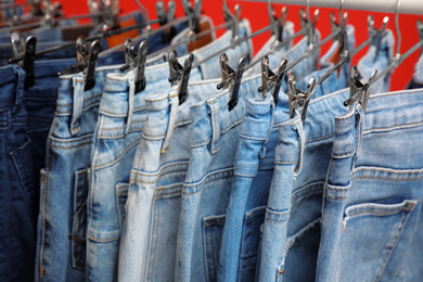 Hangers with stylish jeans on red background, closeup
