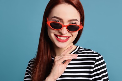 Happy woman with red dyed hair and sunglasses on light blue background