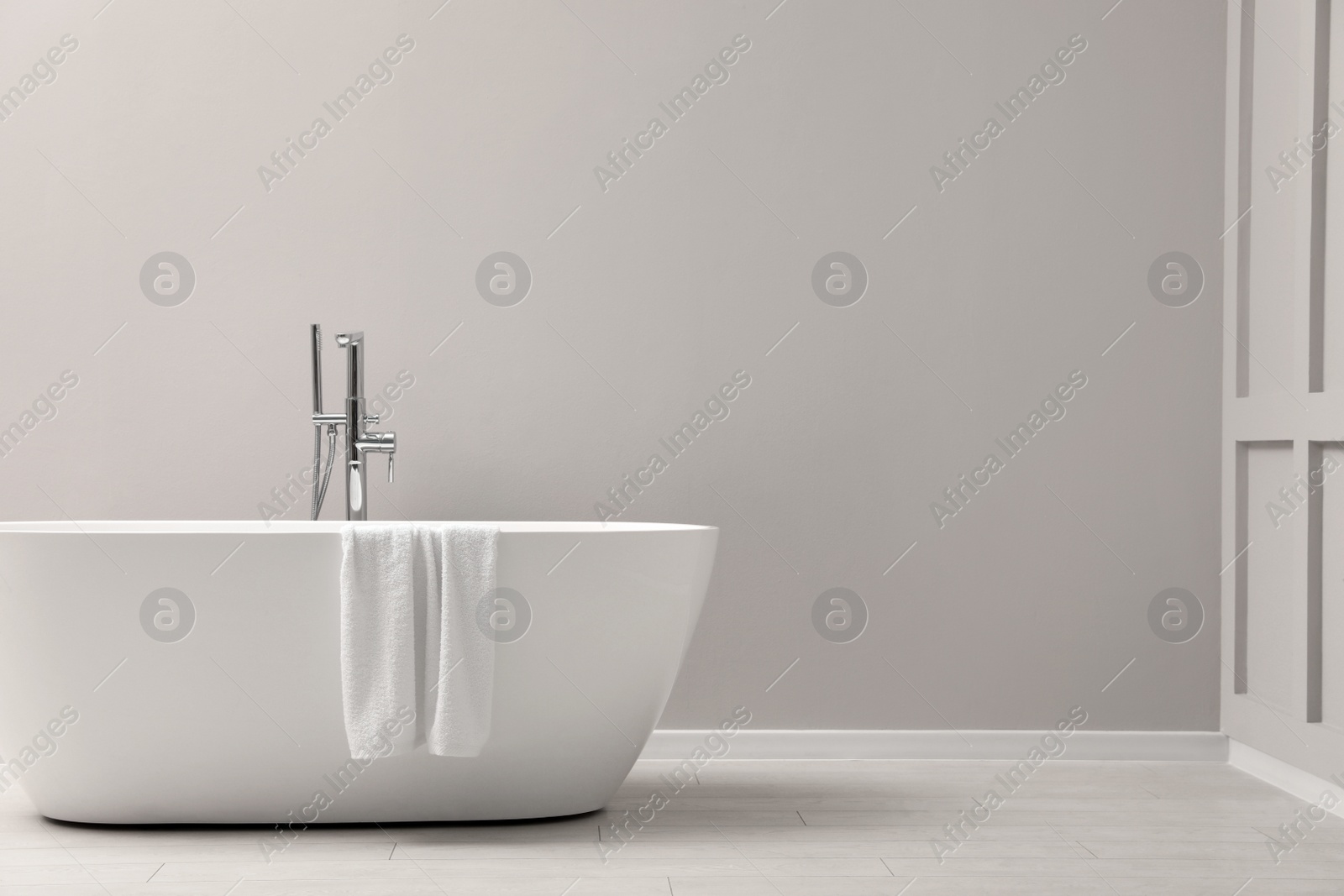 Photo of Modern ceramic bathtub with towel near light wall indoors, space for text