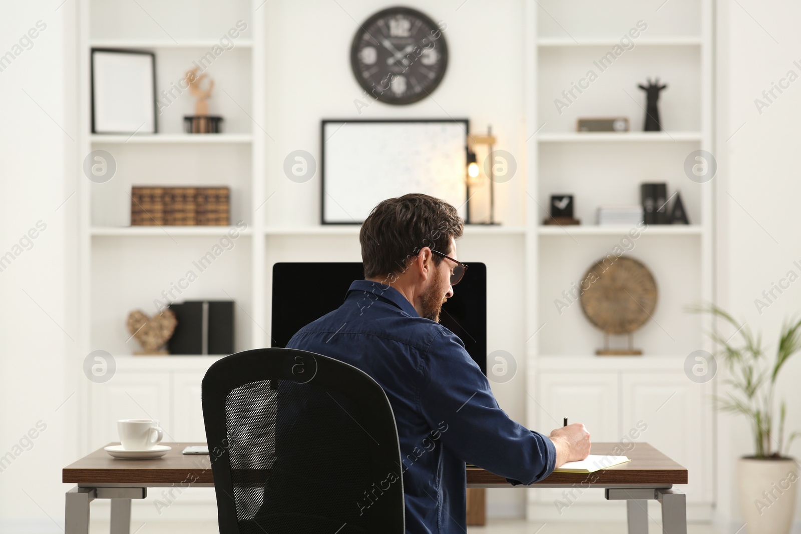 Photo of Home workplace. Man working at wooden desk in room, back view