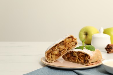 Delicious strudel with apples, nuts and raisins on white table, space for text