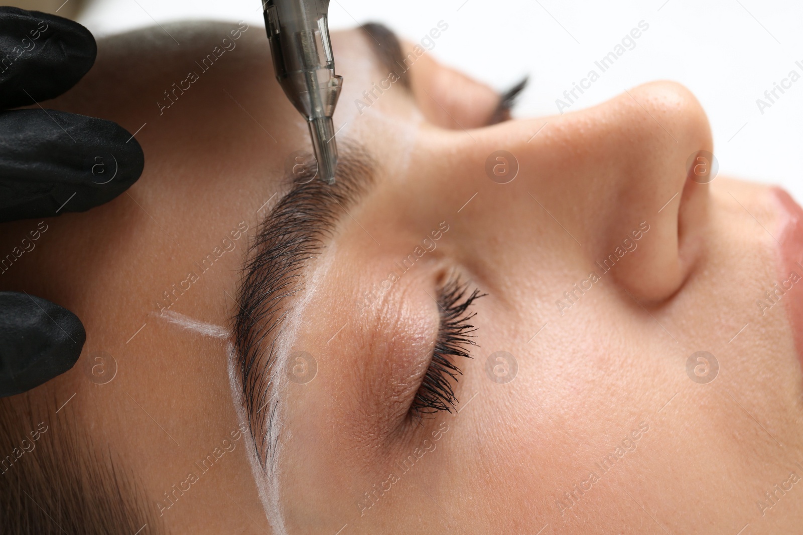 Photo of Beautician making permanent eyebrow makeup to young woman on white background, closeup