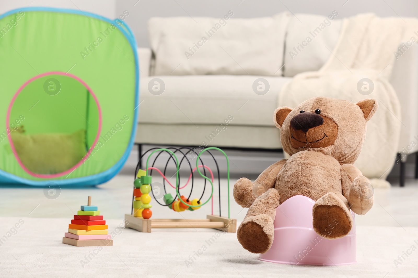 Photo of Cute teddy bear on pink baby potty in room. Toilet training