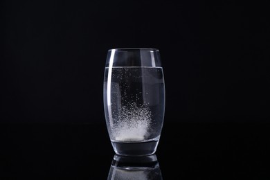 Photo of Effervescent pill dissolving in glass of water on black background