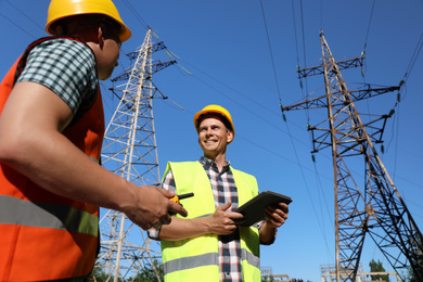 Professional electricians in uniforms near high voltage towers