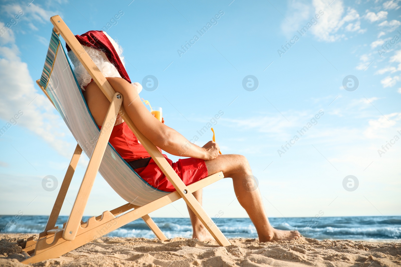 Photo of Santa Claus relaxing in chair on beach, space for text. Christmas vacation