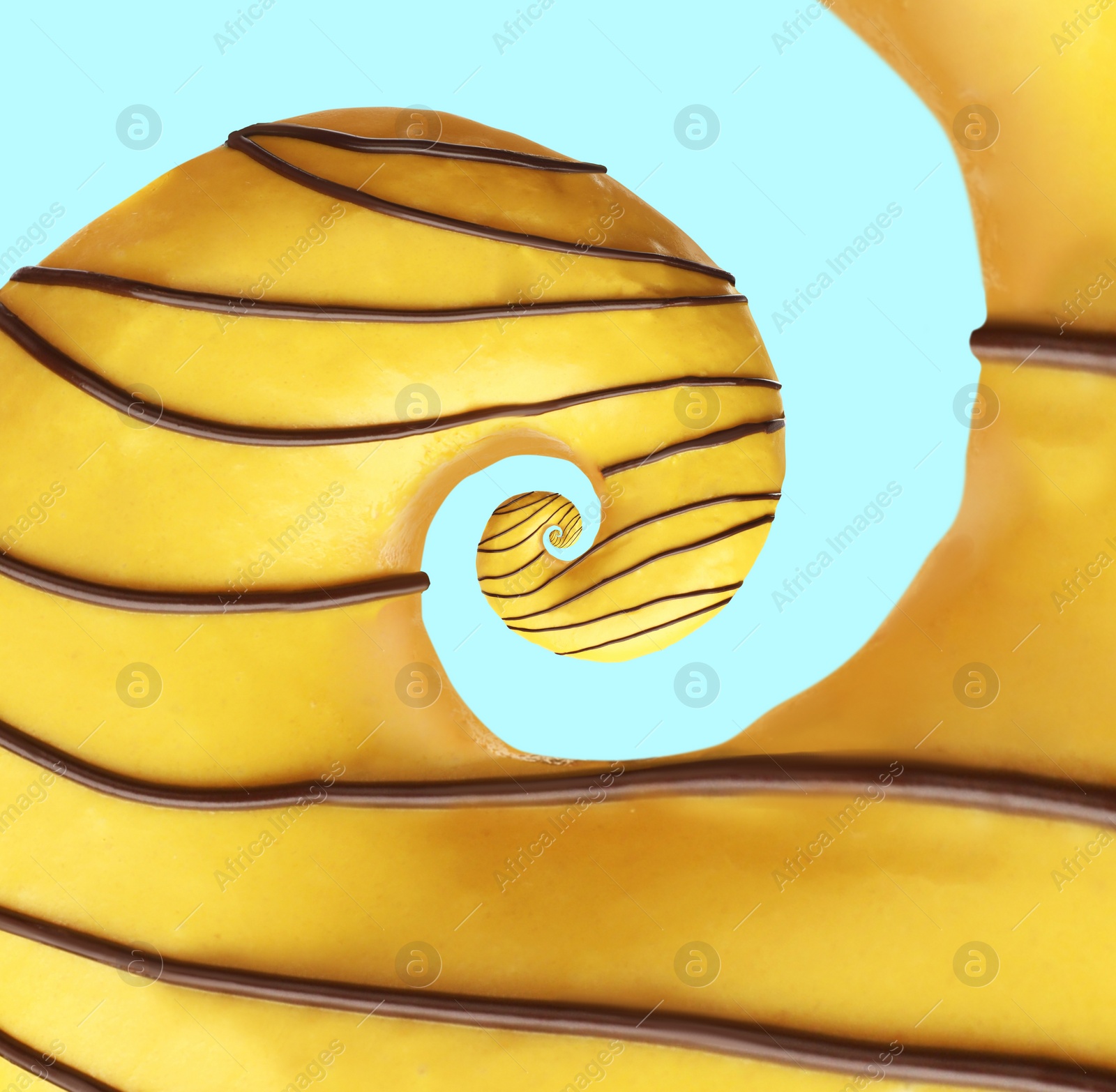 Image of Twisted donut with banana icing and chocolate topping on pale light blue background, spiral effect