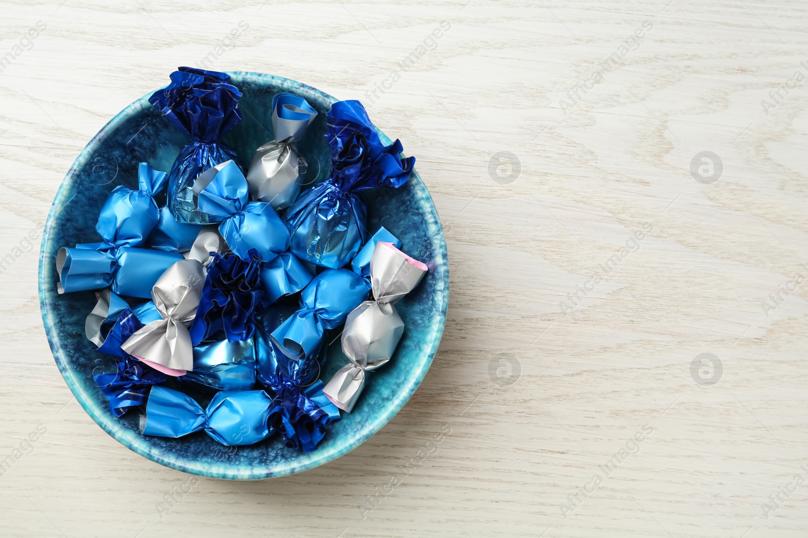 Photo of Candies in colorful wrappers on white wooden table, top view. Space for text