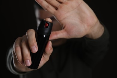 Photo of Man using pepper spray against black background, focus on hands
