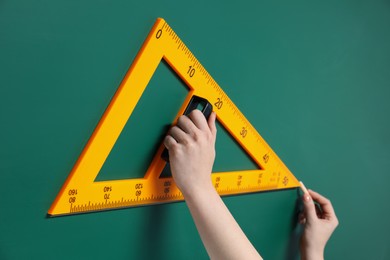 Photo of Woman drawing with chalk and triangle ruler on green board, closeup