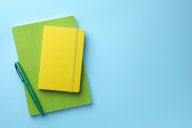 Different notebooks and pen on light blue background, top view. Space for text