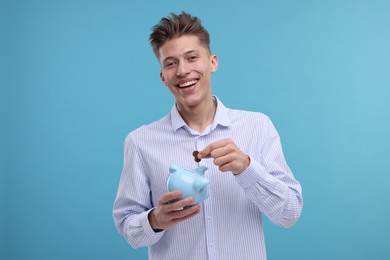 Photo of Happy man putting coins into piggy bank on light blue background