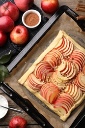 Photo of Baking tray with uncooked apple galette and ingredients on wooden table, flat lay