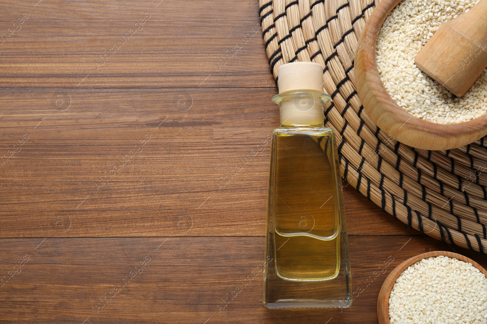 Photo of Fresh sesame oil in glass bottle and seeds on wooden table, flat lay. Space for text