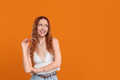 Photo of Stylish young hippie woman with sunglasses on orange background, space for text