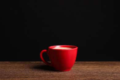 Photo of Red ceramic cup with hot aromatic coffee on wooden table against black background